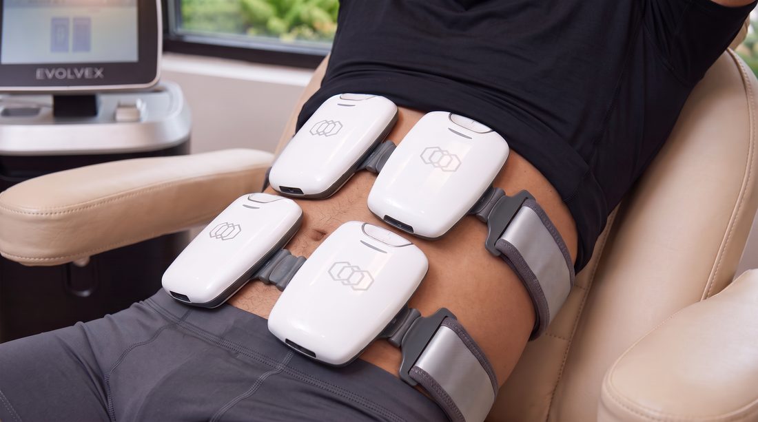 EvolveX applicators strapped across the abdomen and flanks, with the EvolveX console alongside, in a BodyWorks treatment room